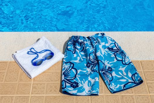 Blue swimming trunks goggles and bath towel at pool