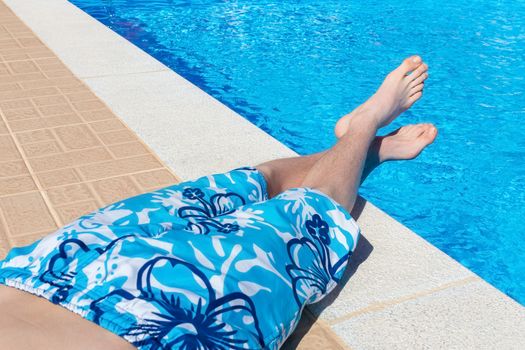 Teenage boy sunbathing at blue swimming pool on vacation in summer season