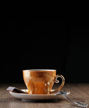 Gold Tea cup with spoon on wood tabe and black background