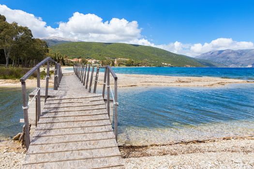 Wooden pedestrian walkway on sunny pebbles beach in greece