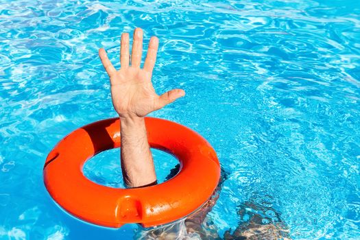 Arm with hand through orange buoy in blue swimming pool
