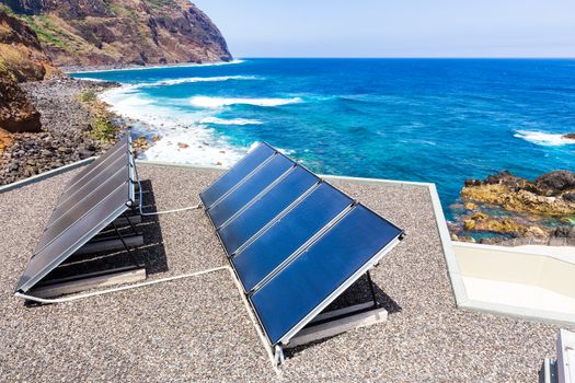 Rows of blue solar panels on house near beach, ocean and mountain