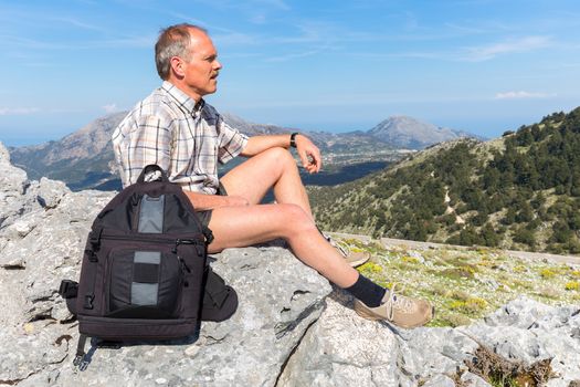 dutch man sitting with backpack in  mountain landscape on sunny day