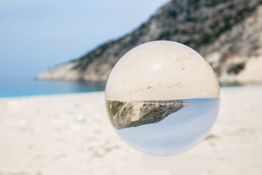 Crystal ball on sandy greek beach with sea and mountain