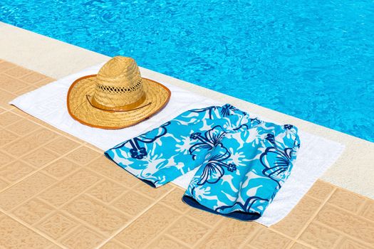 reed hat and swimming trunks on towel near blue fswimming pool