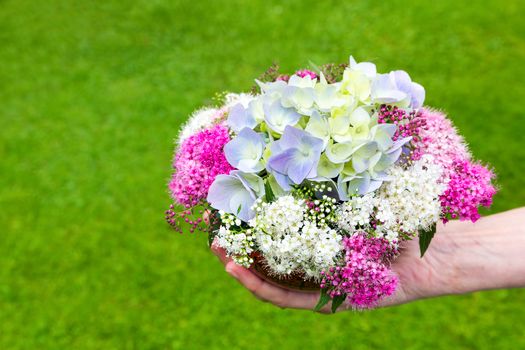 Hand giving bouquet of summer flowers on vase with grass background