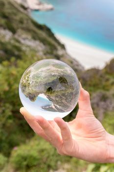 Hand holding crystal ball near sea beach and mountain