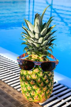 Pineapple wearing sunglassesat swimming pool on sunny day