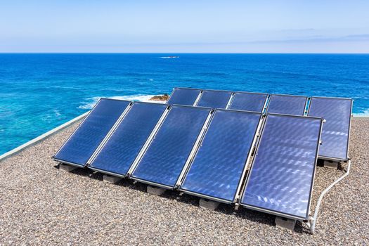 Group of blue solar panels on roof near water of ocean