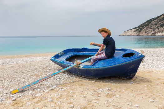 Dutch teenage boy rowing in blue boat on greek beach