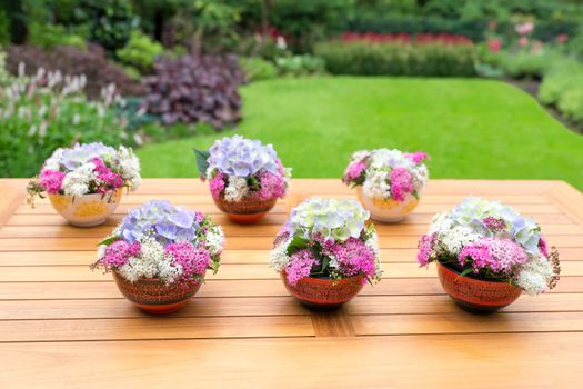 Vases with blossoming flowers on teak table outdoors in garden
