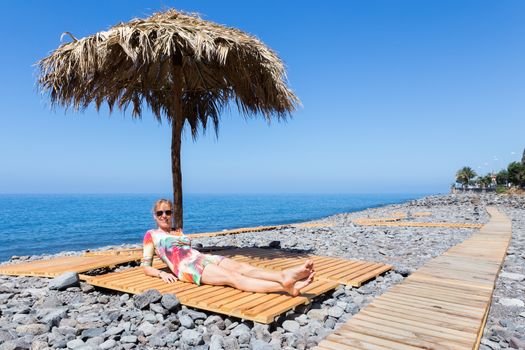 Caucasian middle aged woman sunbathing as tourist on stony  beach in Madeira