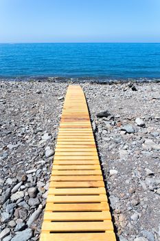 Wooden footpath on grey stony beach leading to portuguese ocean