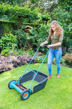 Young caucasian woman pushing lawn mower on grass