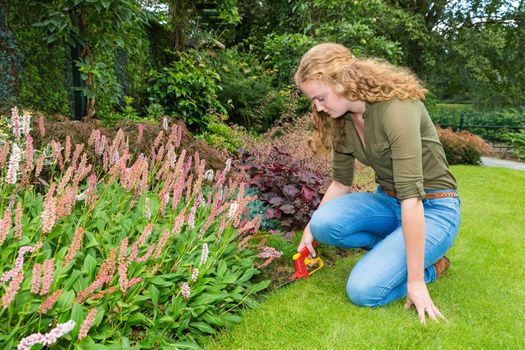 Young caucasian woman works in garden with grass shears