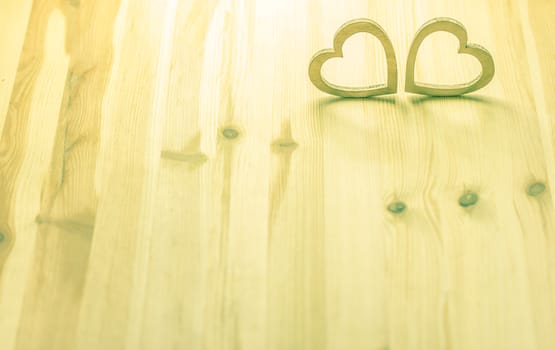 Two hearts, hand carved from wood, in a warm light on a wooden background