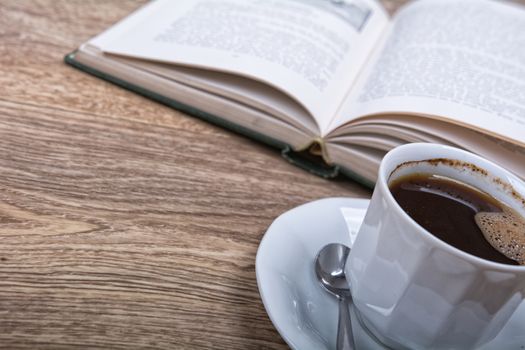 A cup of coffee with a book on a wooden background