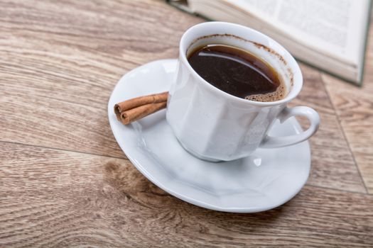 A cup of coffee and cinnamon with a book on a wooden background