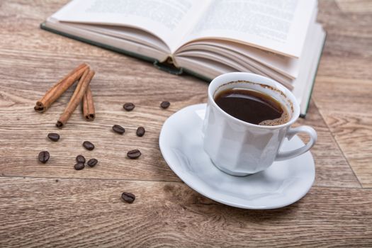 A cup of coffee and cinnamon with a book on a wooden background