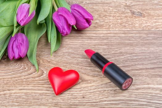 Lipstick, red heart and violet tulips on a wooden background