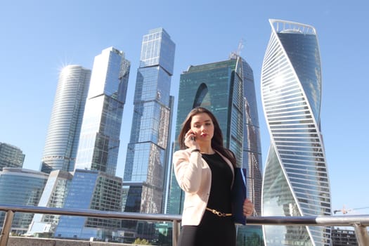 Young beautiful businesswoman with cellphone outdoors at skyscraper background