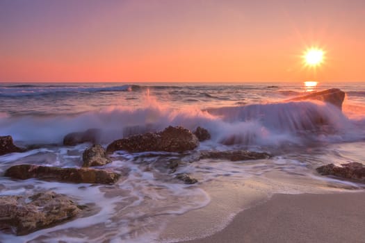 Sea sunrise. Beach and rocks with slow shutter and waves flowing out.