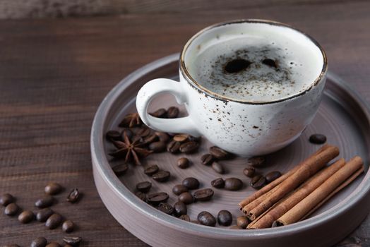 Vintage cup of coffee, coffee beans, star anise and cinnamon in a ceramic tray on a dark brown wooden background