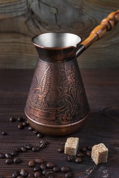 Ancient coffee maker, scattered coffee beans and pieces of sugar cane are on a dark wooden background; vertical image