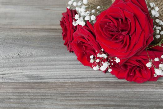 Lonely bouquet of beautiful red roses lying on the gray background of old wooden boards