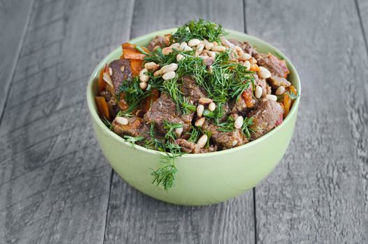 Veal, sauteed with vegetables, sprinkled with herbs and pine nuts. The bowl on the old gray boards.