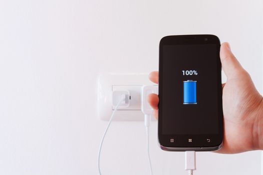 female hand plugging in the wall electtric plug of her smartphone in a socket