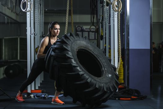 Concept: power, strength, healthy lifestyle, sport. Powerful attractive muscular woman CrossFit trainer doing giant tire workout at the gym