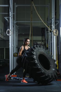 Concept: power, strength, healthy lifestyle, sport. Powerful attractive muscular woman CrossFit trainer doing giant tire workout at the gym