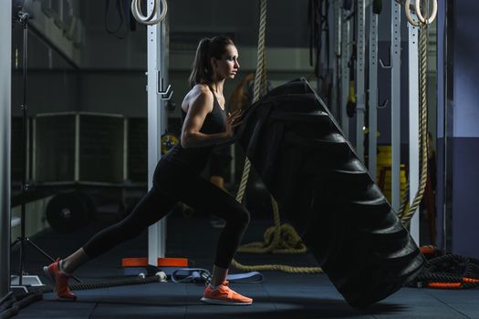 Concept: power, strength, healthy lifestyle, sport. Powerful attractive muscular woman CrossFit trainer doing giant tire workout at the gym