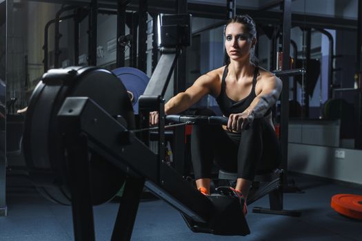 Concept: power, strength, healthy lifestyle, sport. Powerful attractive muscular woman CrossFit trainer do workout on indoor rower at the gym