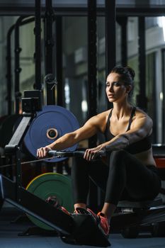 Concept: power, strength, healthy lifestyle, sport. Powerful attractive muscular woman CrossFit trainer do workout on indoor rower at the gym