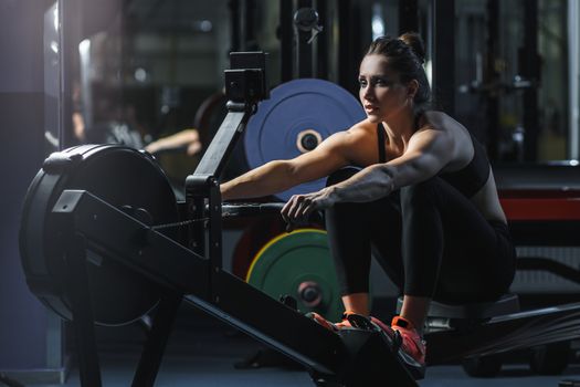 Concept: power, strength, healthy lifestyle, sport. Powerful attractive muscular woman CrossFit trainer do workout on indoor rower at the gym