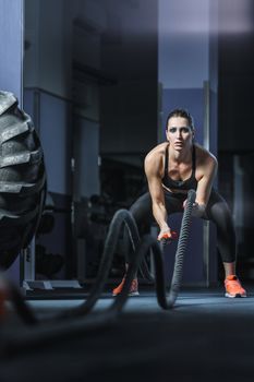 Concept: power, strength, healthy lifestyle, sport. Powerful attractive muscular woman CrossFit trainer do battle workout with ropes at the gym