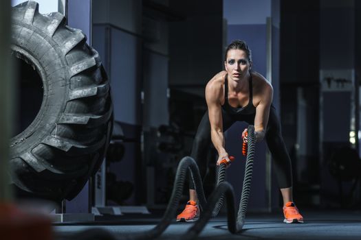 Concept: power, strength, healthy lifestyle, sport. Powerful attractive muscular woman CrossFit trainer do battle workout with ropes at the gym