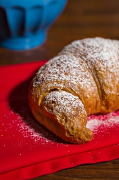 Closeup of a croissant over a red napkin and a blue mug on background