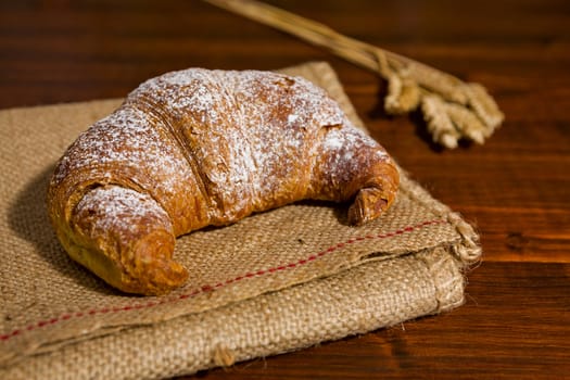 Croissant on a burlap and ears of wheat over a table
