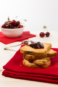 Rusk with cherry jam over a red napkin and cherry fruit on background