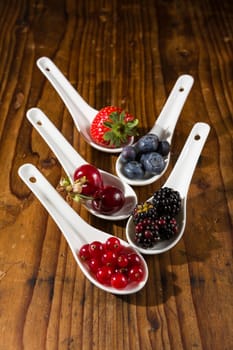 Collection of wild berries on white spoons over a wooden background