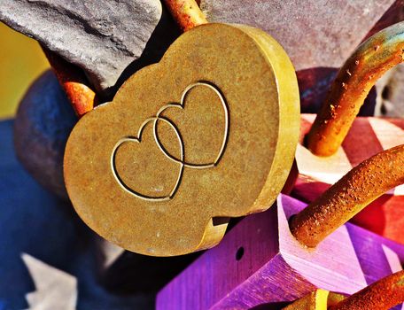 Padlock with two joined hearts engraved on it, attached to the railing of the brigde. There are also a few more colorful and rusty padlocks next to. Love padlocks are very popular form of expressing love by lovers, especially tourists visiting famous places and bridges of love. Photo was taken in Hamburg, Germany.