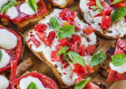 Creamy cheese over crispy toasts topped with tomatoes and basil. Horizontal image.