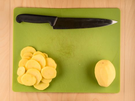 Whole and sliced peeled potatoe on used green plastic board with knife, simple food preparation illustration, vegetarian dieting, top view still life