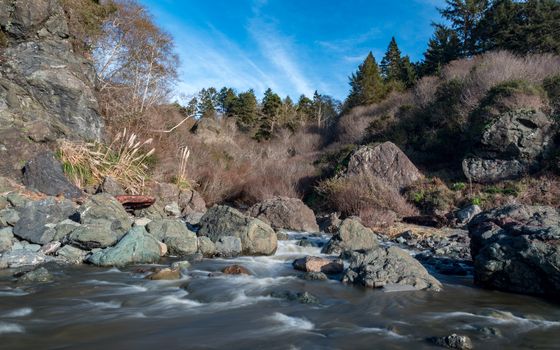 Long-exposure image of a river flowing over rocks and under a blue sky.