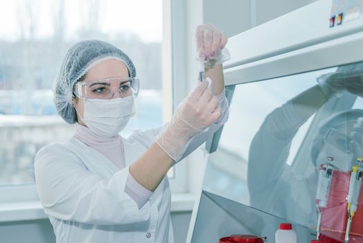 Woman scientist in a white protective clothing conducts research in a real lab