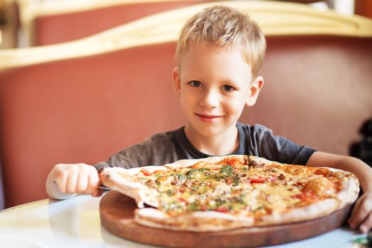 Children eat Italian pizza in the cafe. Adorable little boy eating pizza at a restaurant