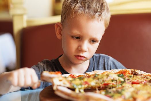 Children eat Italian pizza in the cafe. Adorable little boy eating pizza at a restaurant